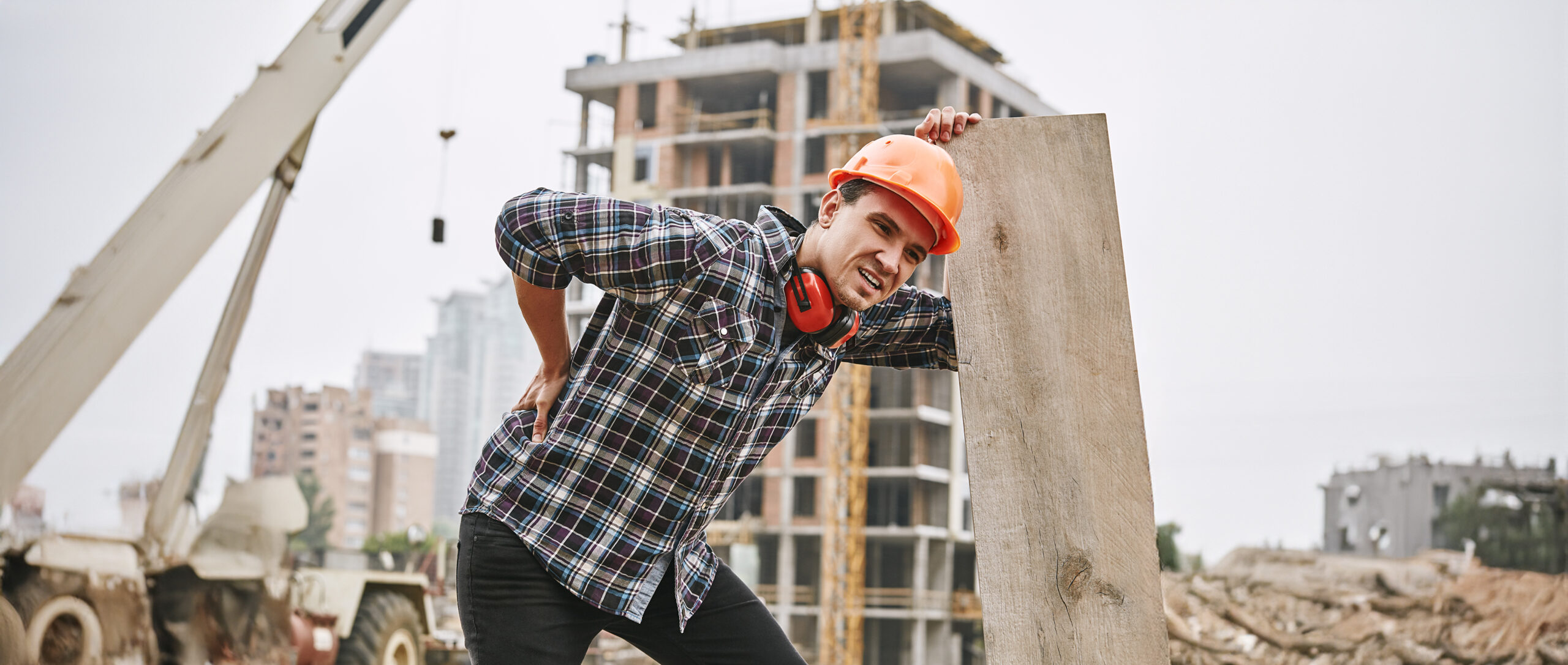 Construction worker in protective helmet feeling back pain while working at construction site